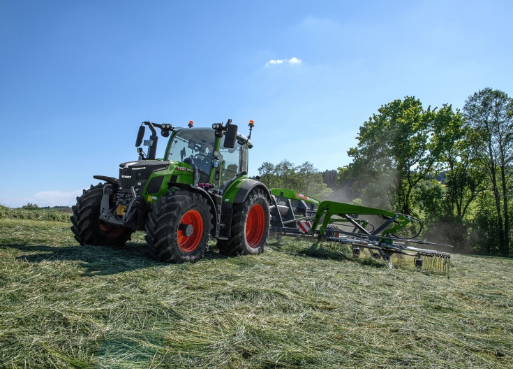 Ένα πράσινο Fendt 500 Vario οδηγεί με κεντρική τσουγκράνα Fendt Former πάνω από ένα κουρεμένο χωράφι και σκαλίζει με τσουγκράνα.