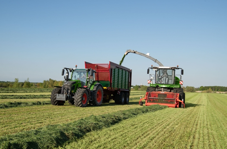 Ένα πράσινο Fendt 500 Vario ρυμουλκεί ένα ρυμουλκούμενο ώθησης της Strautmann δίπλα σε μια πράσινη θεριζοαλωνιστική μηχανή της Fendt. Αυτό κόβει γρασίδι.